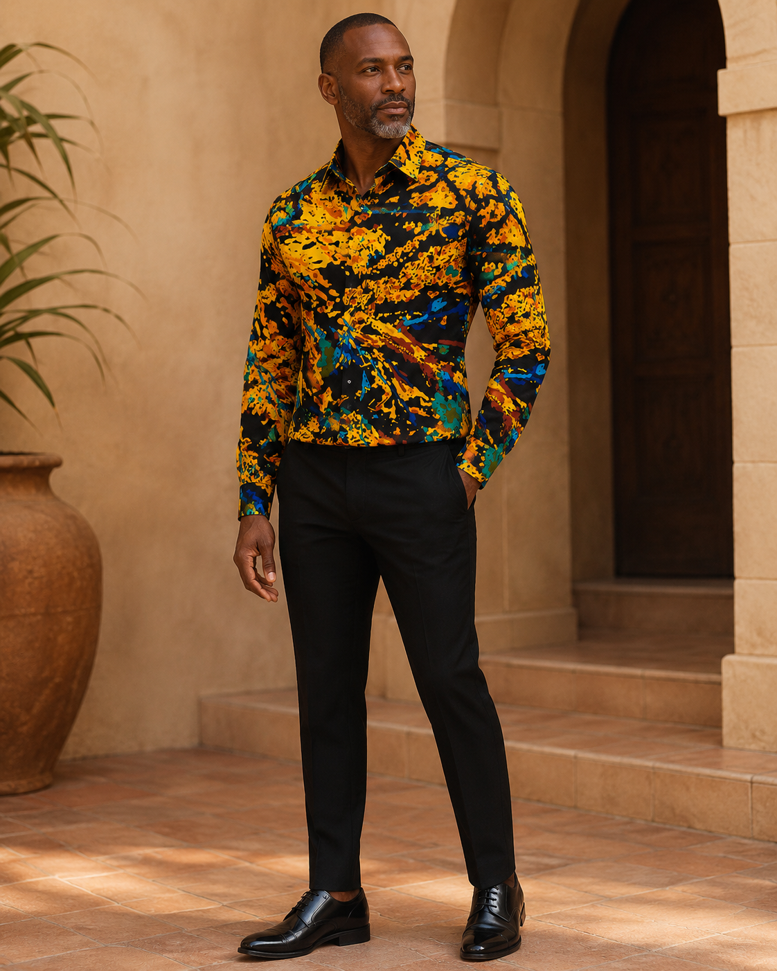 Man wearing a colorful patterned shirt and black pants standing in a sunlit outdoor setting.