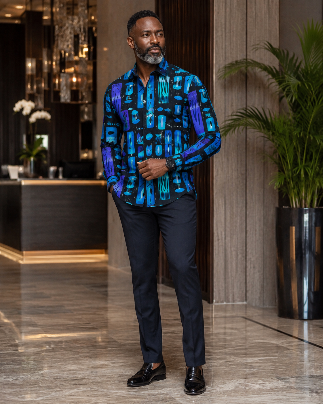 Man wearing a patterned blue shirt and black pants in an indoor setting.