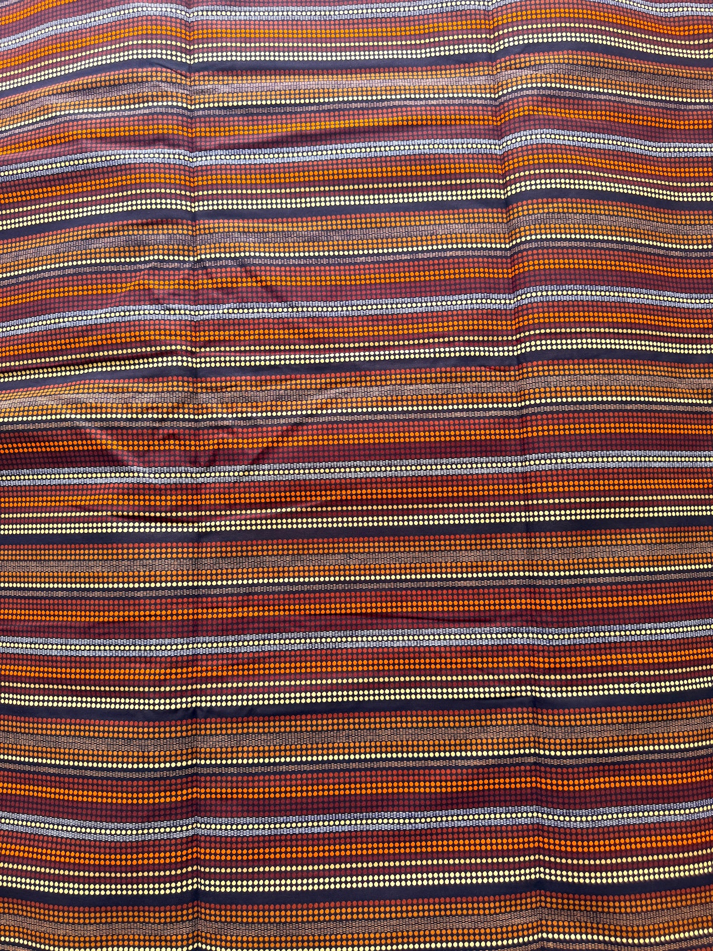 A close-up of a striped woven textile with horizontal bands in orange, brown, beige, white, and dark navy, showing a subtle diamond pattern.
