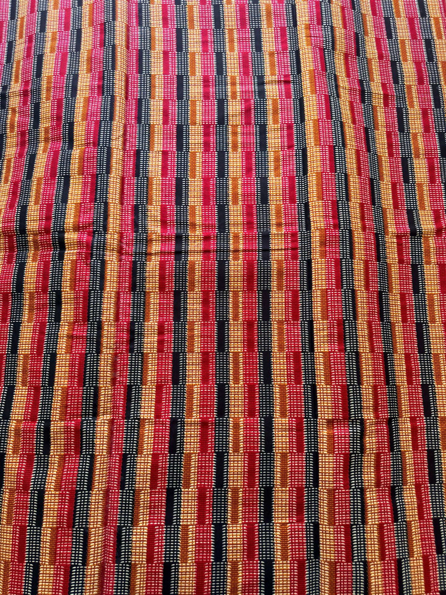 A close-up of a woven textile with a vertical striped pattern in red, orange, yellow, black, and pink.