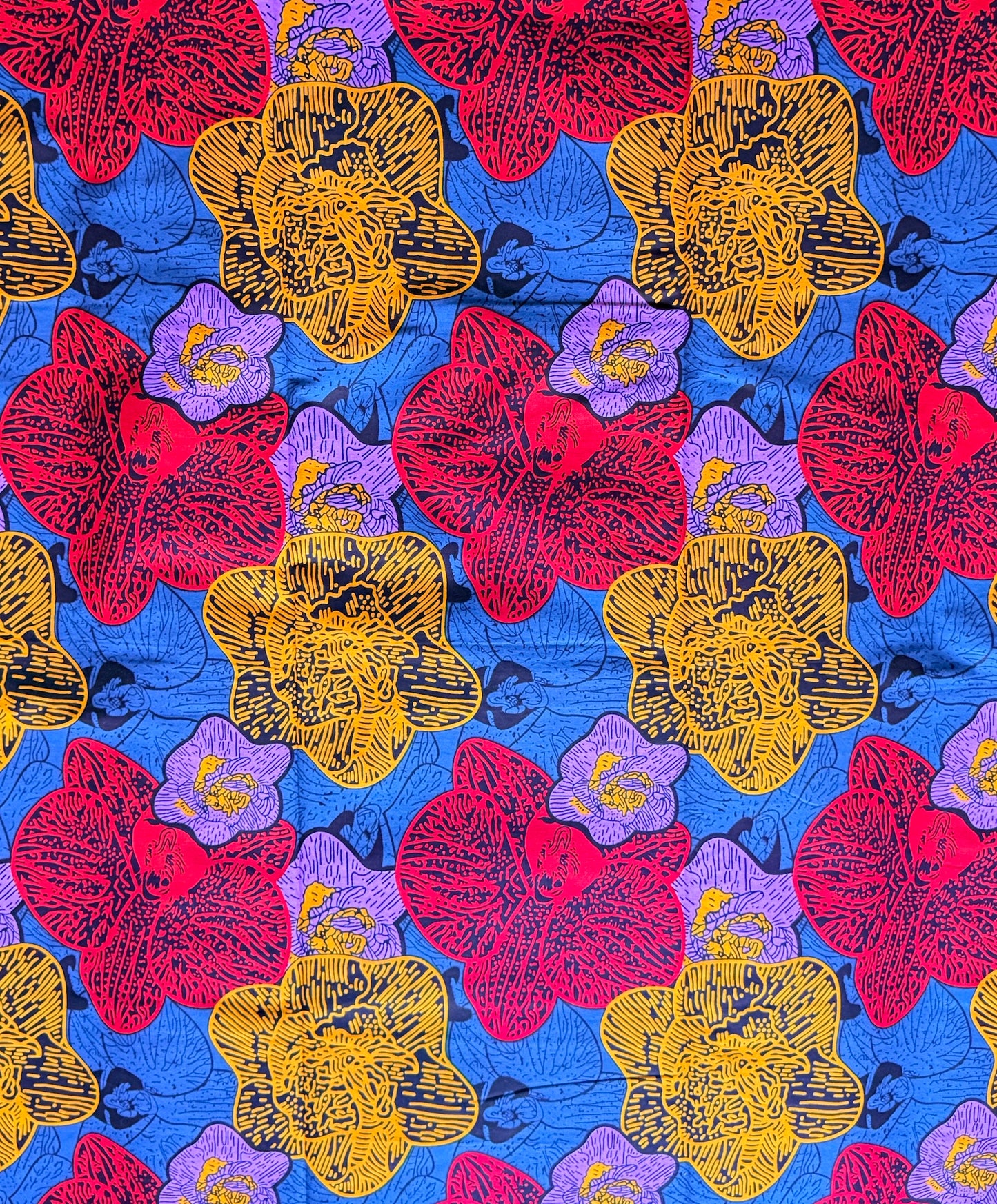 A close-up of a colorful floral fabric pattern featuring large red, yellow, and purple flowers on a bright blue background.