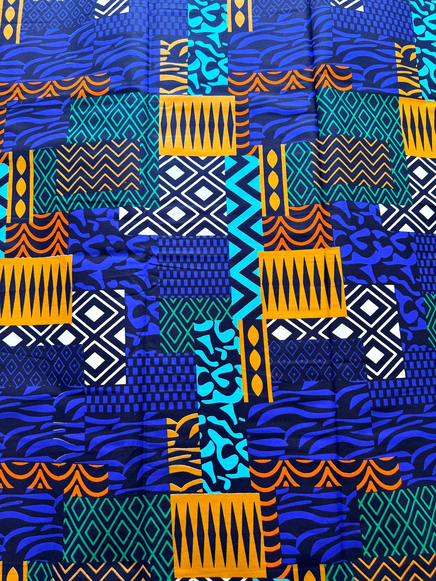 A close-up of a vibrant, multicolored patchwork fabric featuring various geometric and tribal patterns in blue, teal, orange, and white.