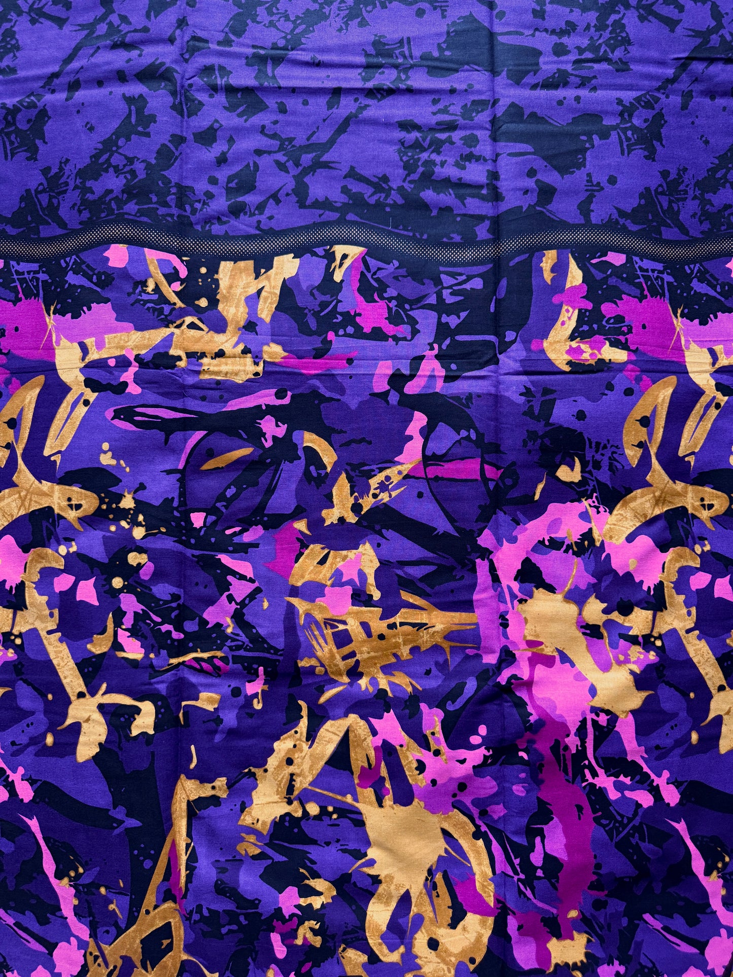 A close-up of a patterned fabric or material featuring an abstract design with a dark navy blue top section and a lower section in purple, magenta, and gold with paint splatter and brushstroke motifs.