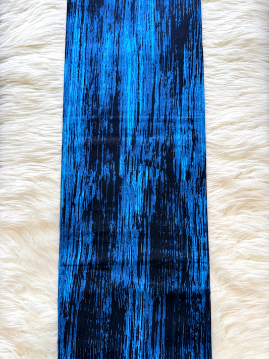 A long rectangular scarf or fabric panel with a vertical blue and black distressed brushstroke pattern, laid flat on a white faux-fur surface.