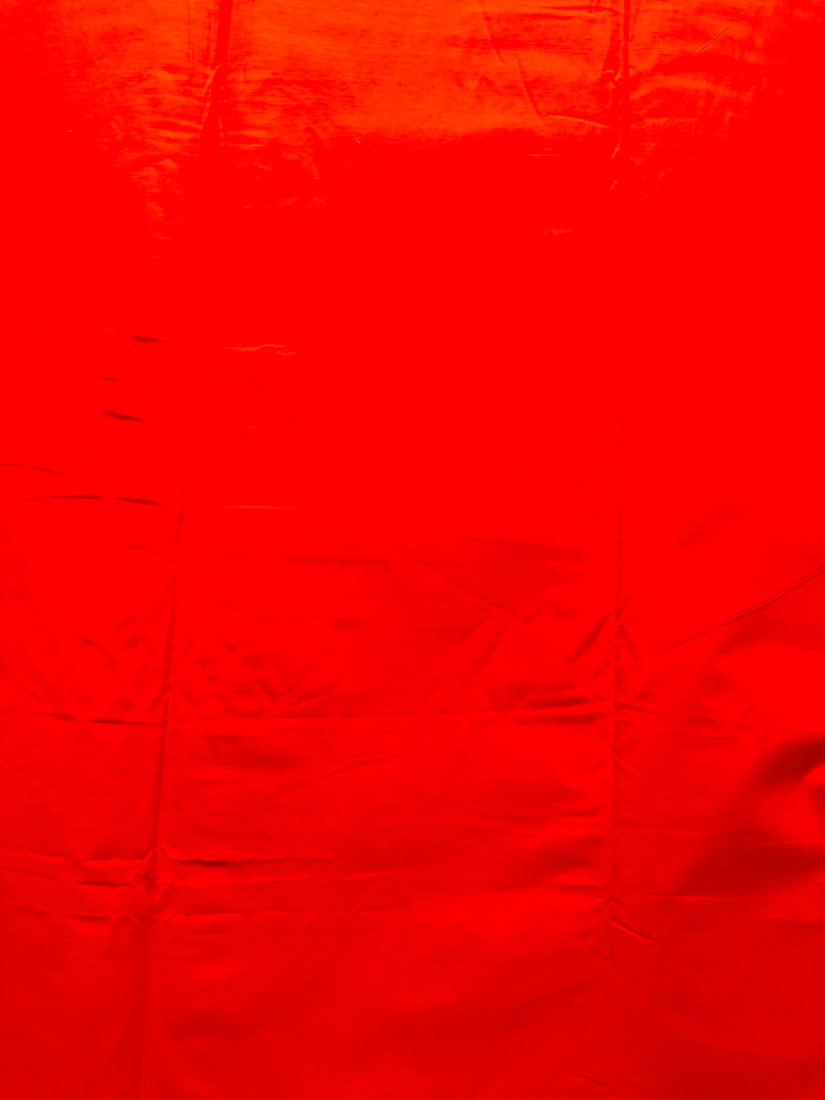 A close-up of bright red fabric with visible folds and a slightly shiny texture filling the frame.