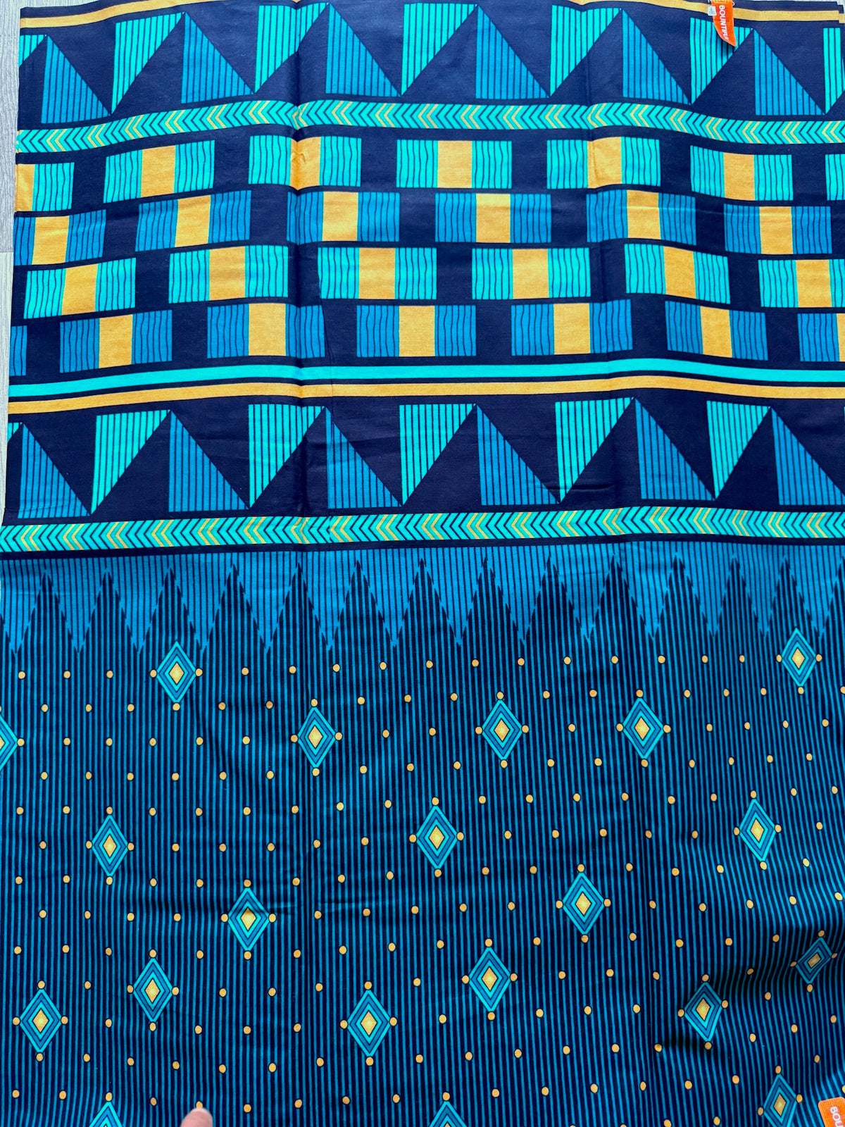 A close-up of a blue patterned textile, likely a sari, featuring geometric and ikat-inspired designs in blue, teal, and yellow.