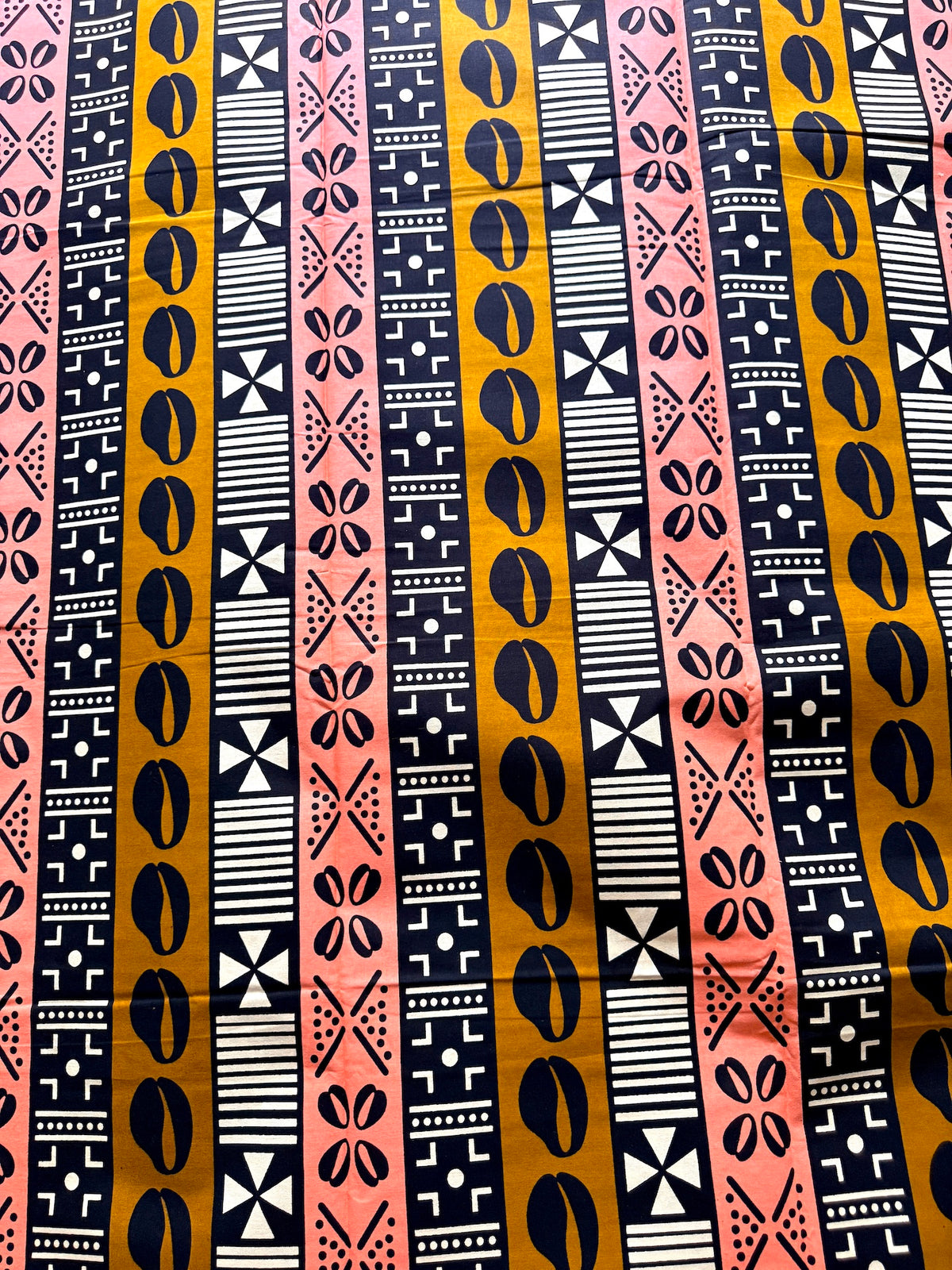 A close-up of a fabric or wallpaper pattern featuring vertical stripes in black, mustard yellow, pink, and white with geometric and tribal-inspired motifs.