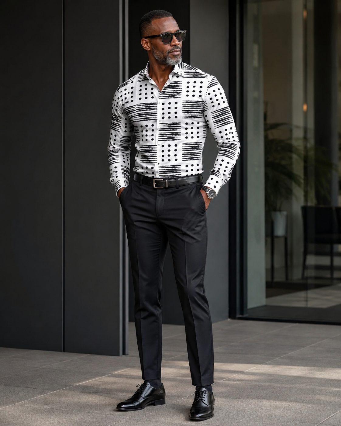 Man wearing a patterned shirt and black pants standing outdoors.