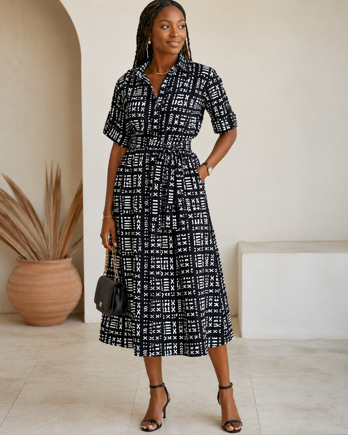 Woman wearing a black and white patterned dress standing in a room with a plant and framed picture.