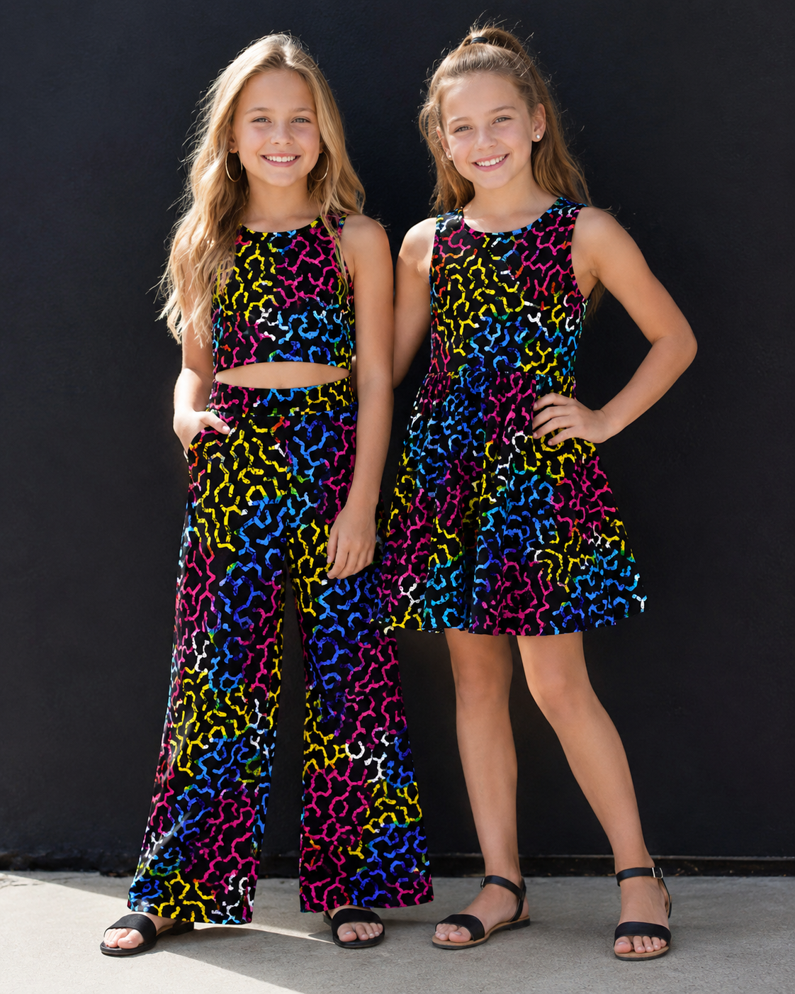 Two young girls wearing colorful leopard print outfits against a black background