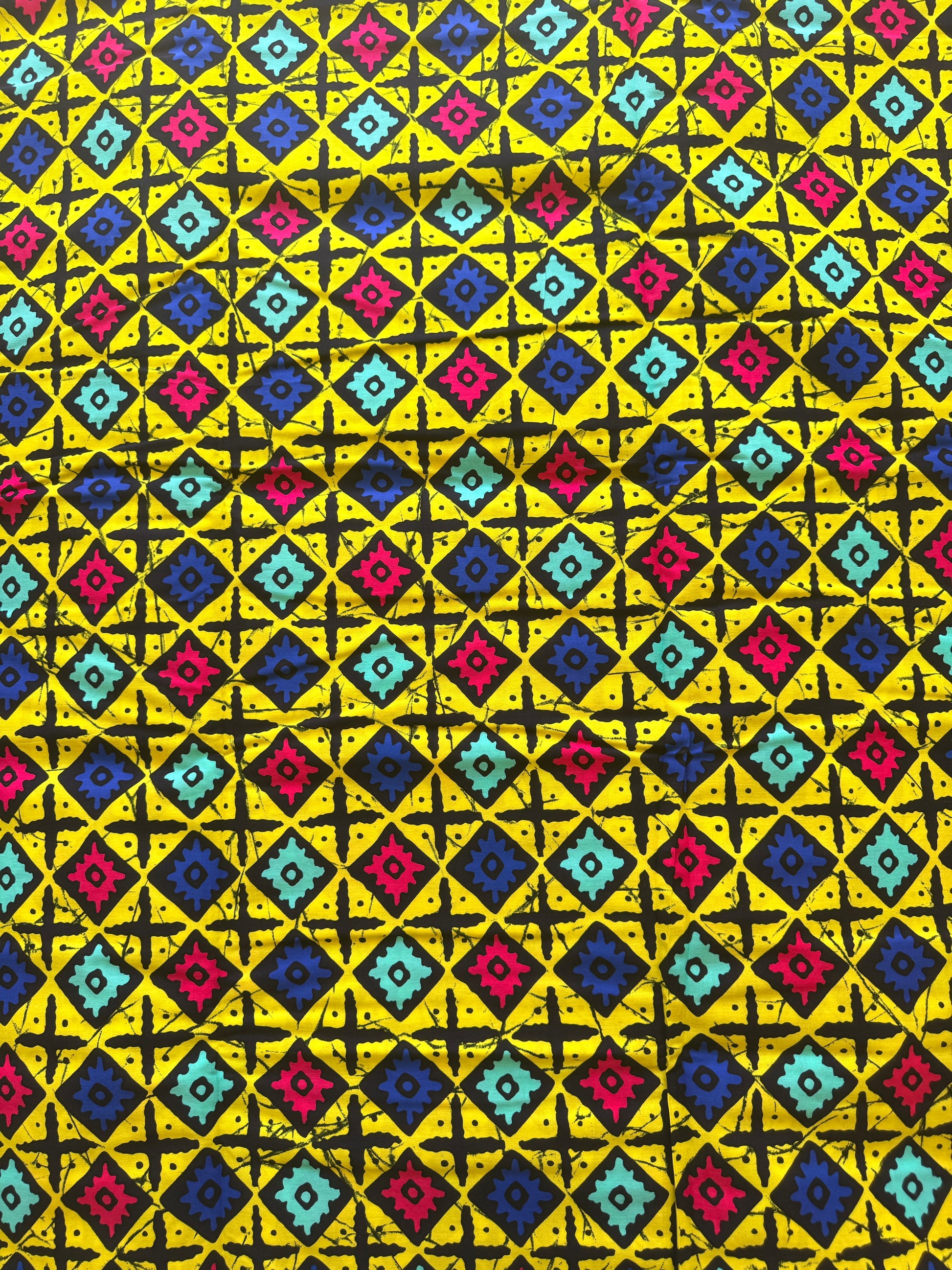 A close-up of a fabric or wallpaper pattern featuring a bright yellow background with a repeating geometric design of black crosses and nested diamonds in blue, pink, and turquoise.