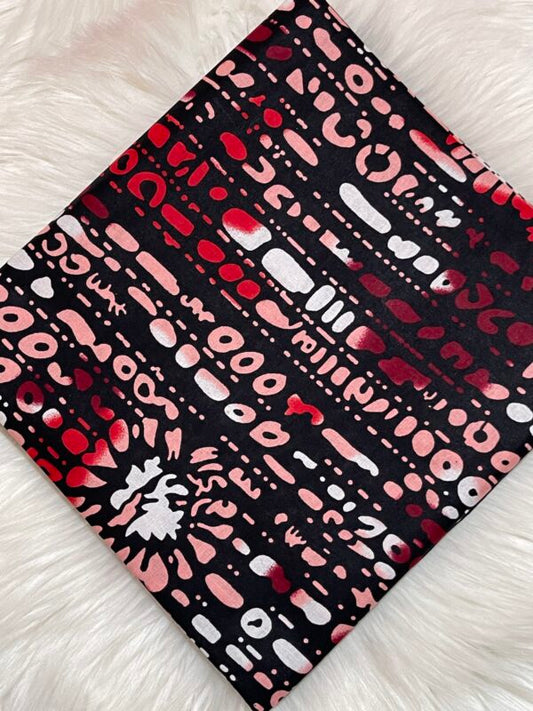 Patterned fabric with red, pink, and white shapes on a black background, laid flat on a white surface.