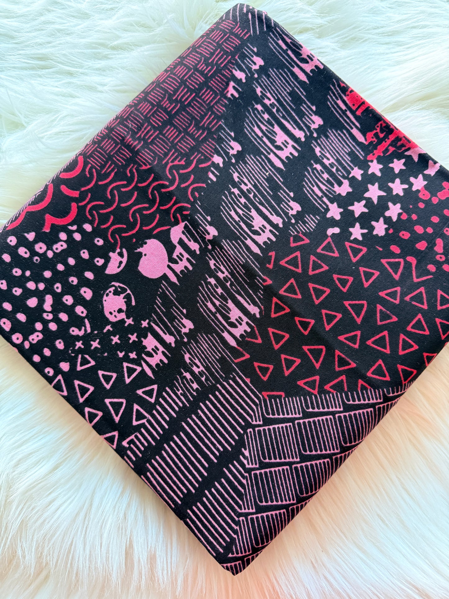 Folded black fabric with pink geometric patterns on a white fluffy surface
