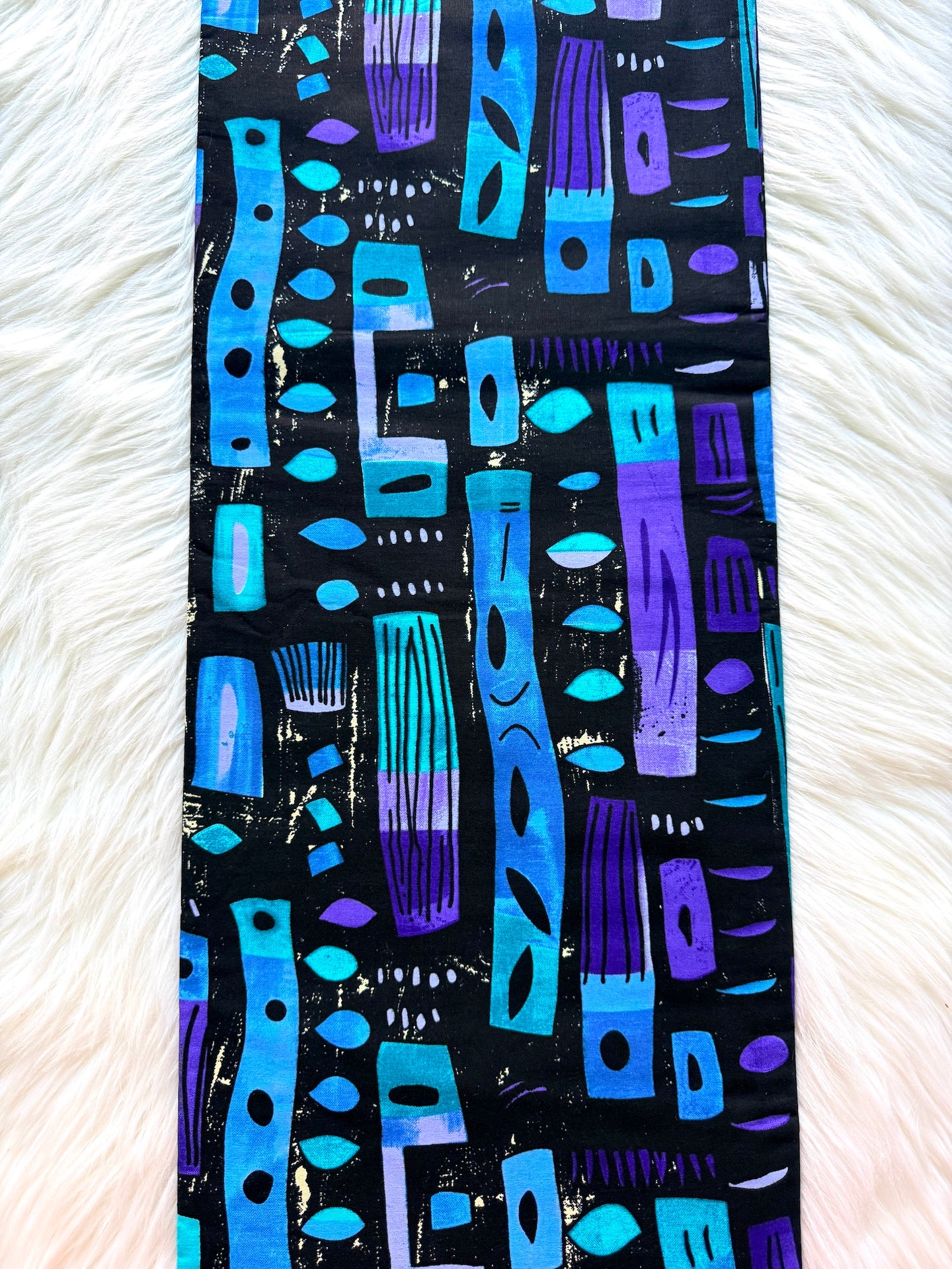 Colorful patterned fabric with blue and purple designs on a black background, placed on a white textured surface.