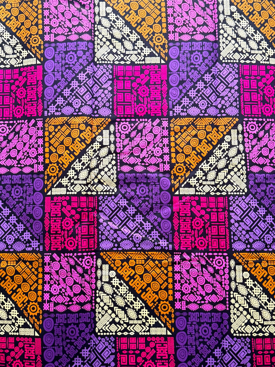 Patterned fabric with geometric design in purple, orange, and pink on a purple background