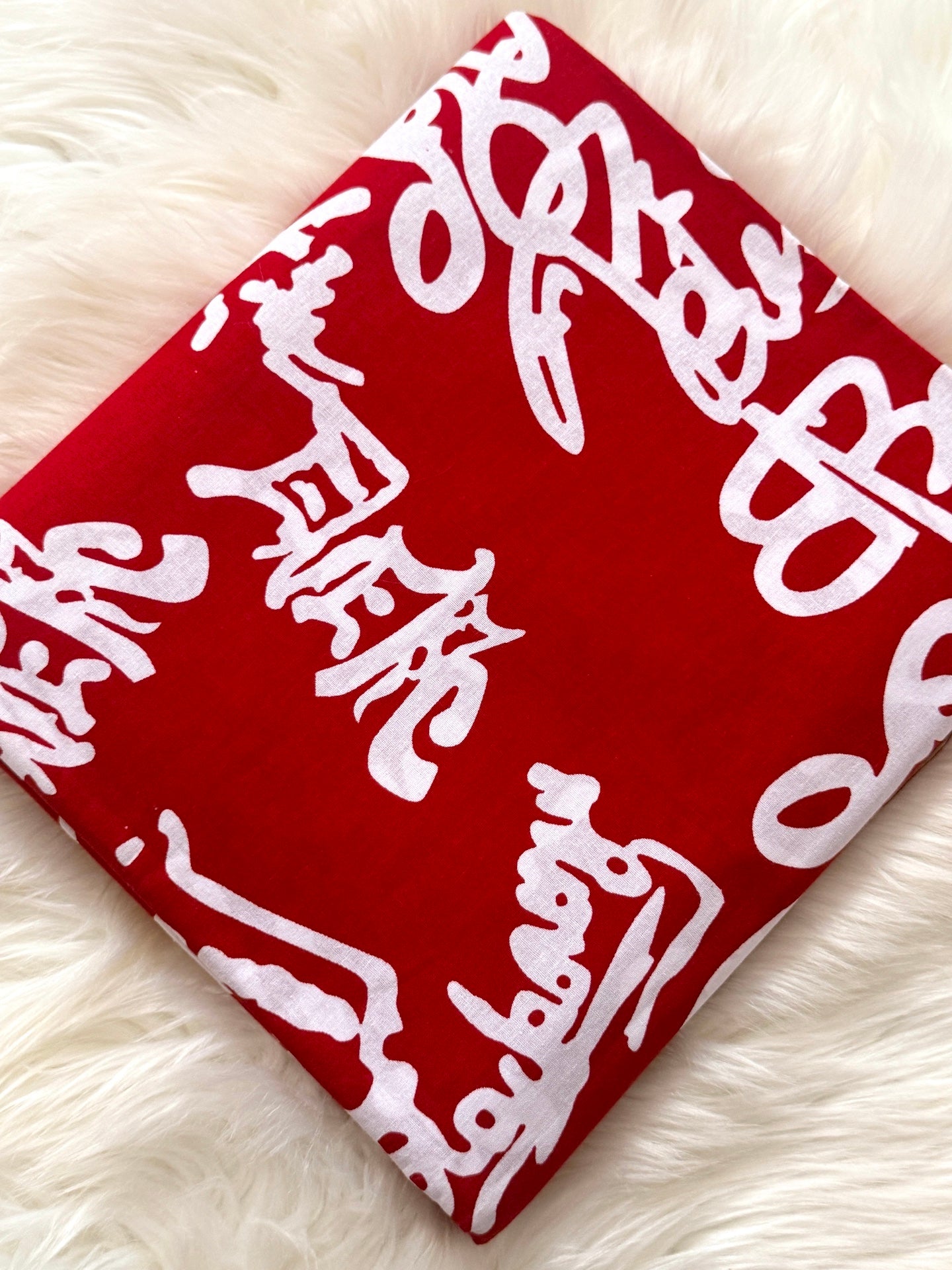 Red bandana with white text and symbols on a white fluffy surface