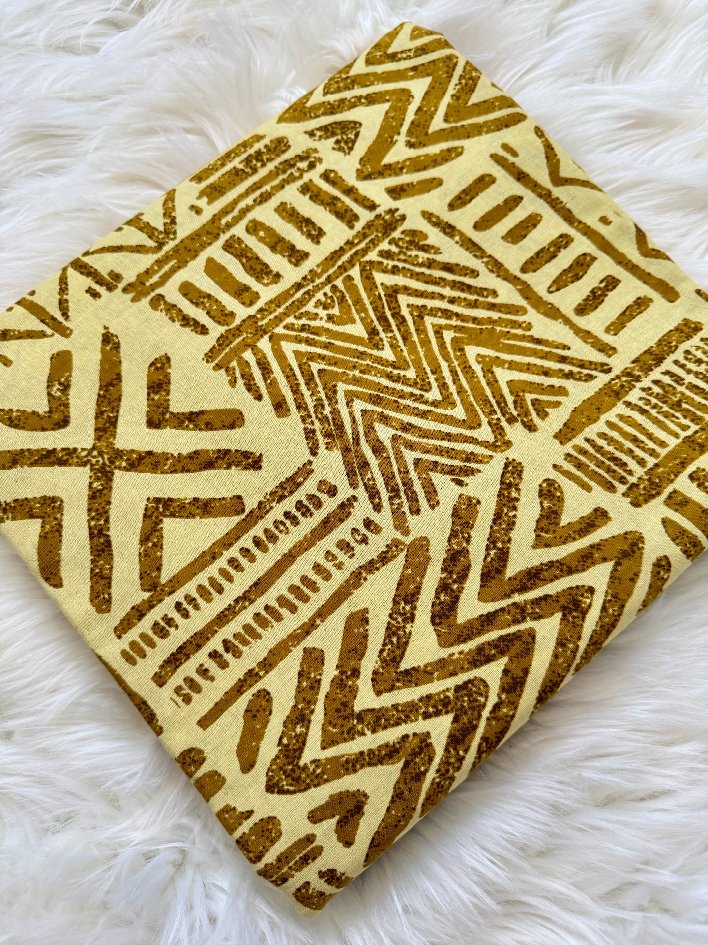Decorative square pillow with gold geometric pattern on a white fluffy surface