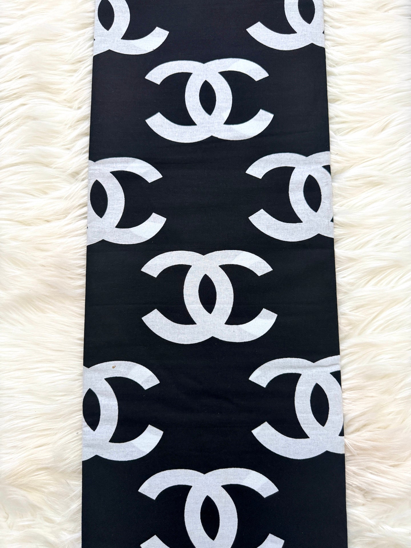 Black scarf with white Chanel logo pattern on a white fluffy surface