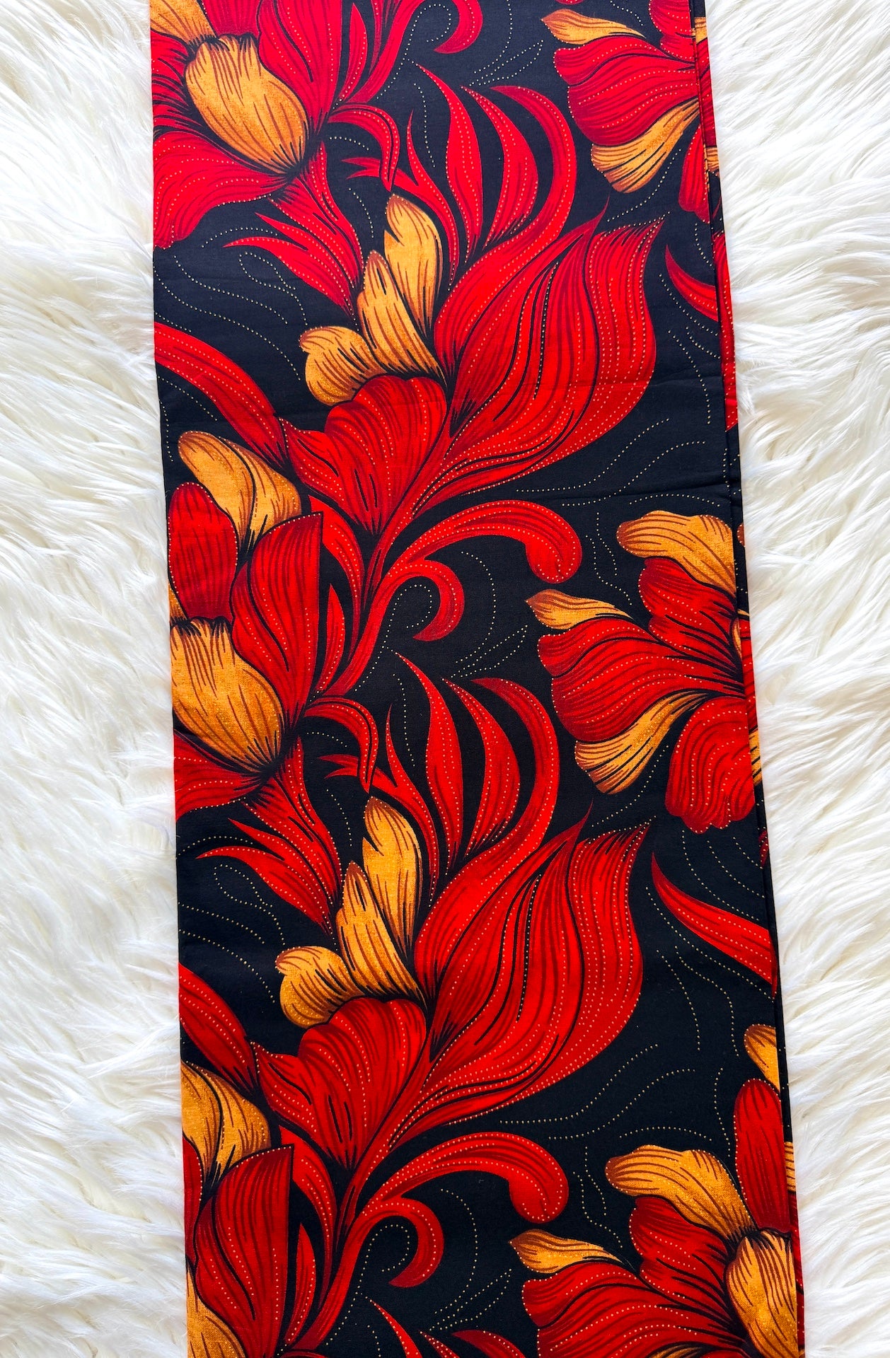 A close-up of a patterned fabric or wallpaper panel featuring bold red and orange floral motifs on a black background, laid flat on a white faux fur surface.