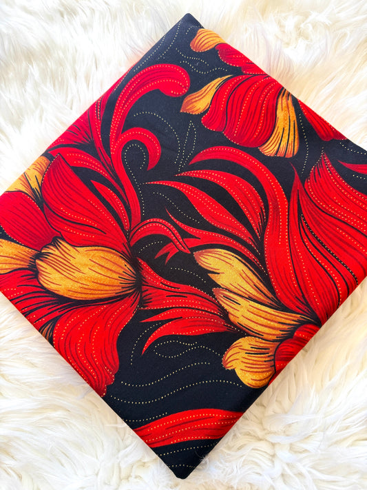 A square fabric item, likely a pillow cover or small blanket, featuring a bold floral pattern in vibrant red and yellow on a black background, laid flat on a white faux fur surface.