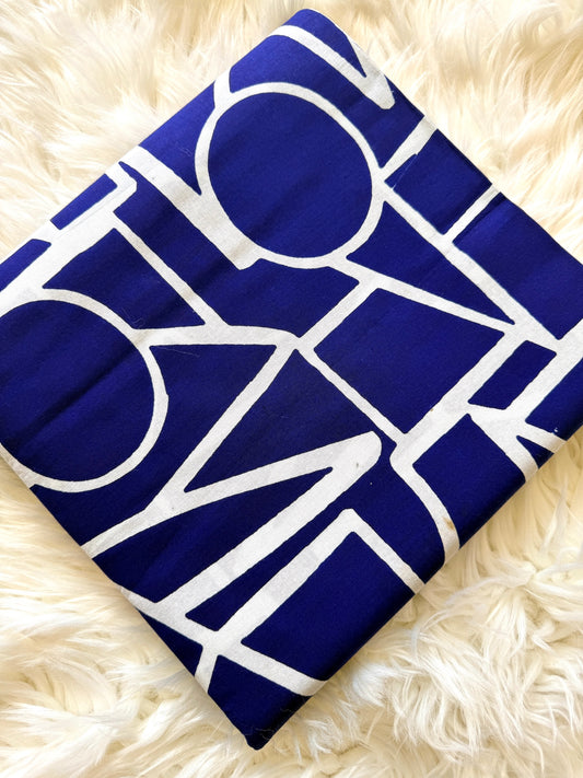 A folded square textile, likely a blanket or throw, featuring a bold geometric pattern in deep blue and white, laid flat on a fluffy cream faux fur surface.