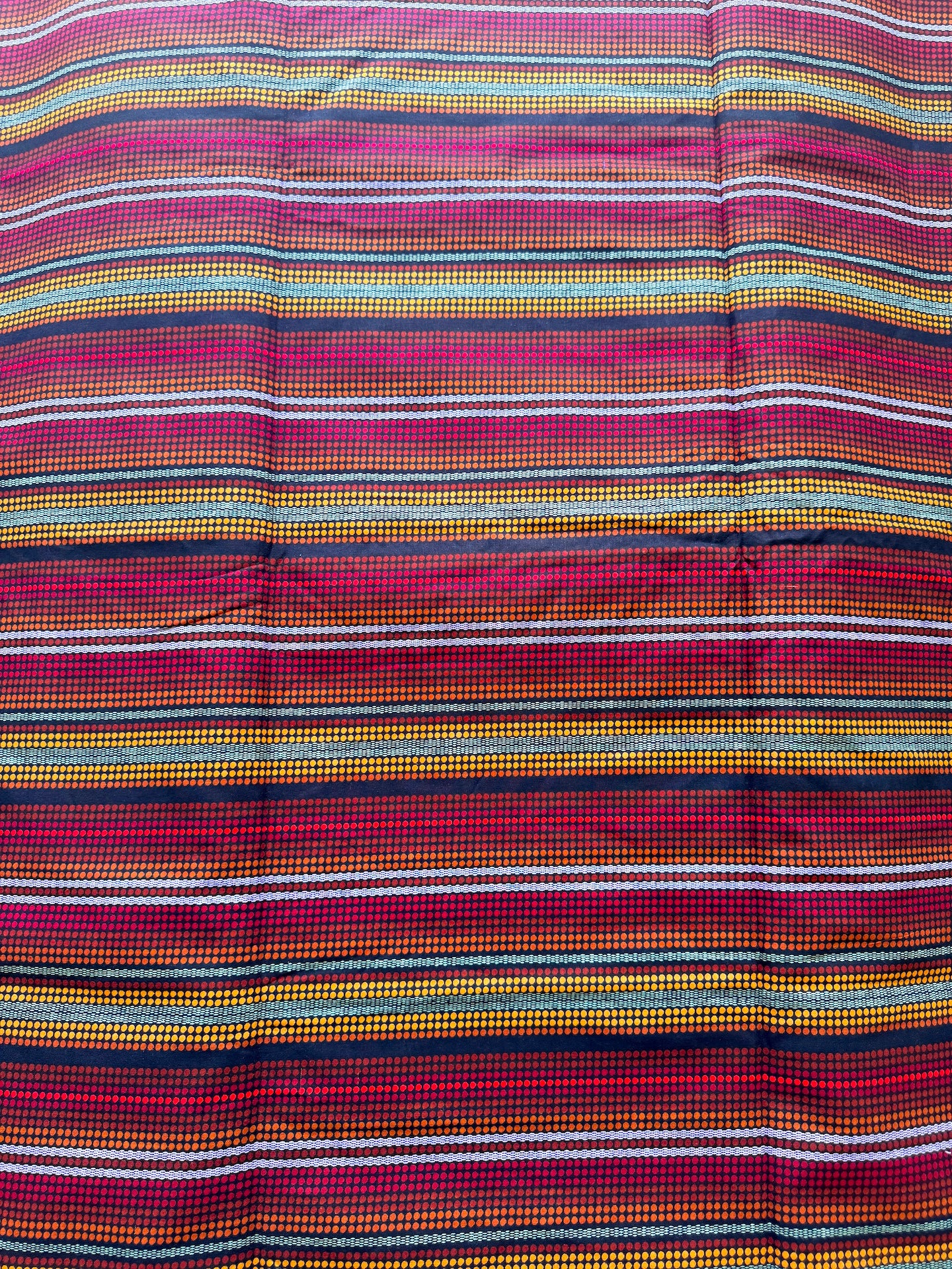A close-up of a striped textile with horizontal bands of red, pink, orange, yellow, white, and dark navy, showing a woven texture.