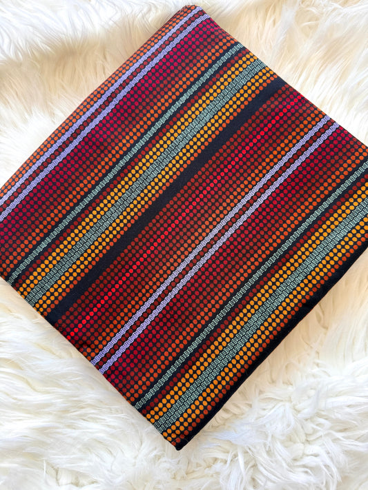 A folded woven textile with a multicolor striped pattern of red, orange, yellow, black, and white, displayed on a white faux fur surface.