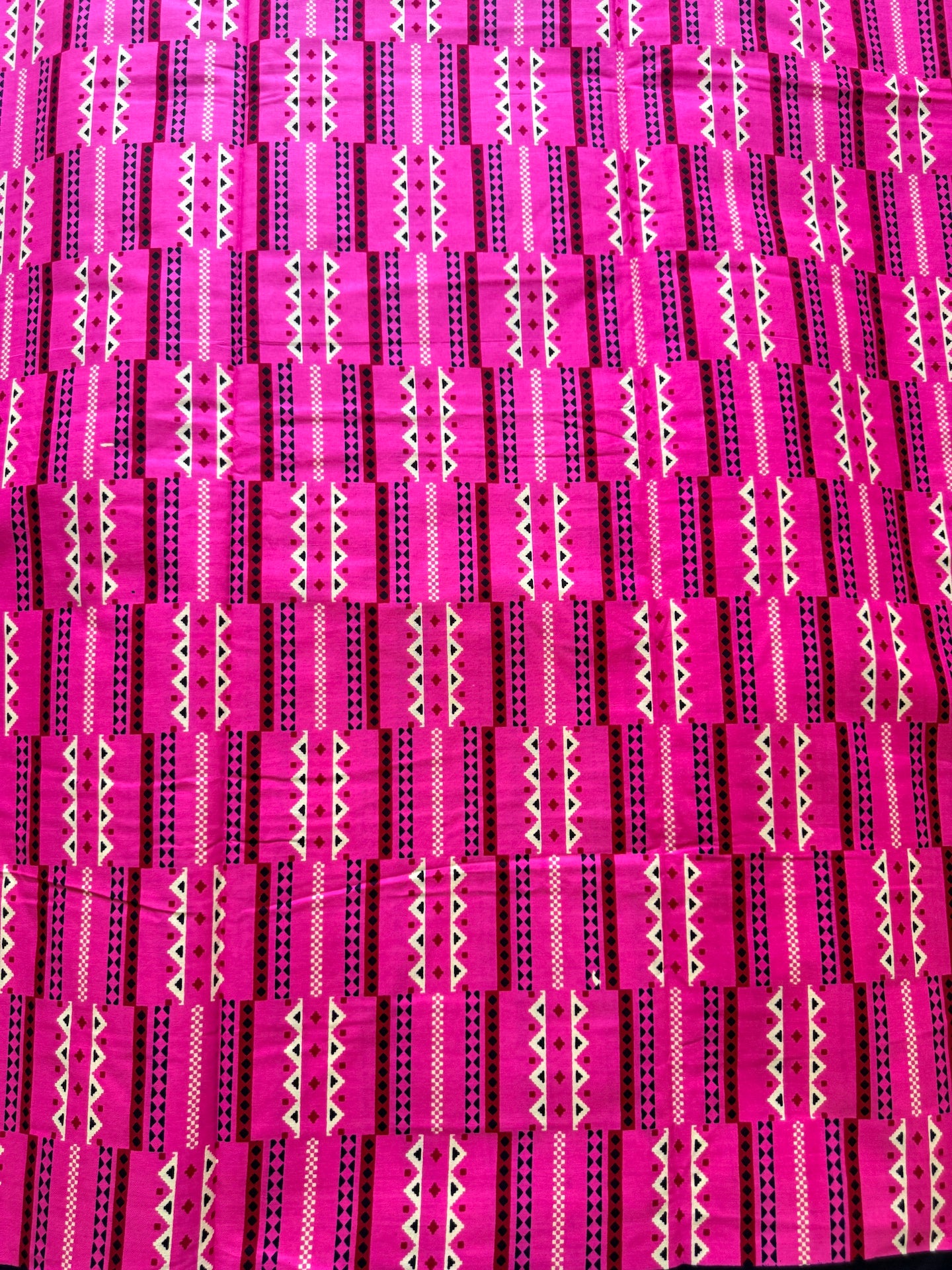 Bright pink and magenta fabric with a repeating geometric pattern of black, white, and dark pink vertical stripes and zigzag motifs.