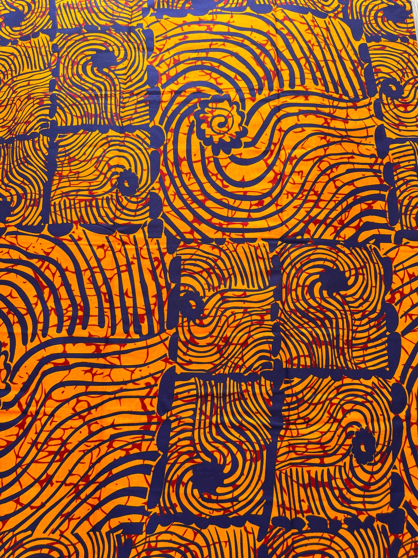 A close-up of a patterned fabric featuring a bold geometric design with orange, navy blue, and red details.
