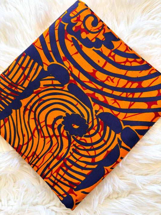A square piece of vibrant orange and navy blue patterned fabric with red accents, laid flat on a white faux fur surface.