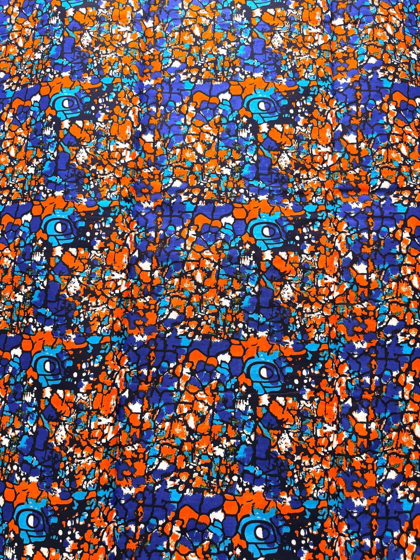 A close-up of a vibrant, multicolored abstract patterned fabric featuring orange, blue, purple, and white shapes outlined in black.