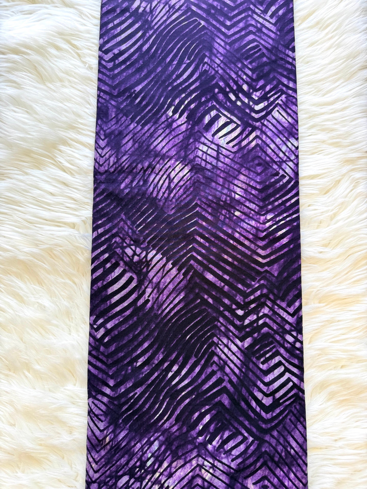 A purple and black patterned scarf laid flat on a white faux fur background.