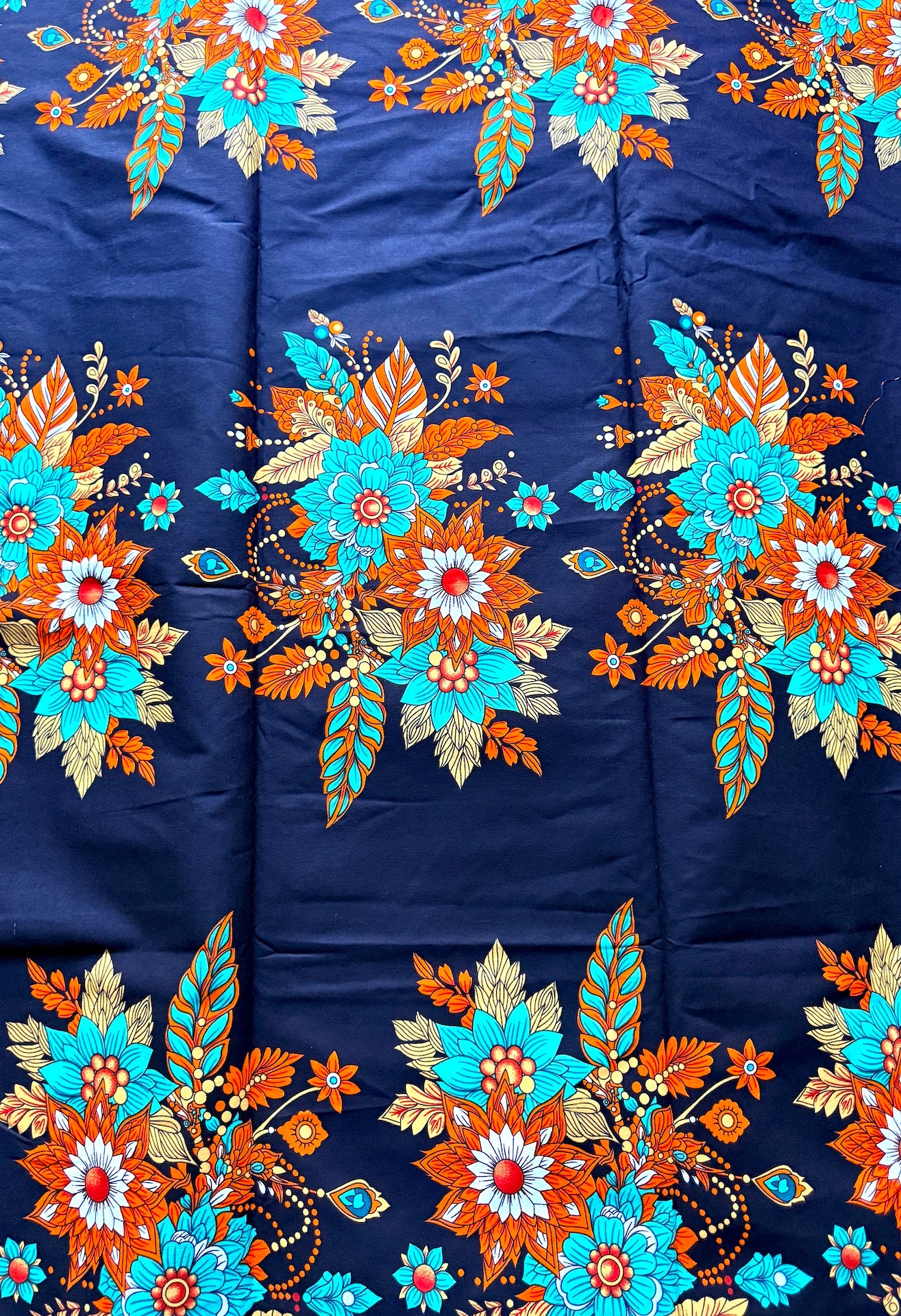 A close-up of a navy blue fabric with vibrant, repeating floral embroidery in orange, turquoise, and gold.