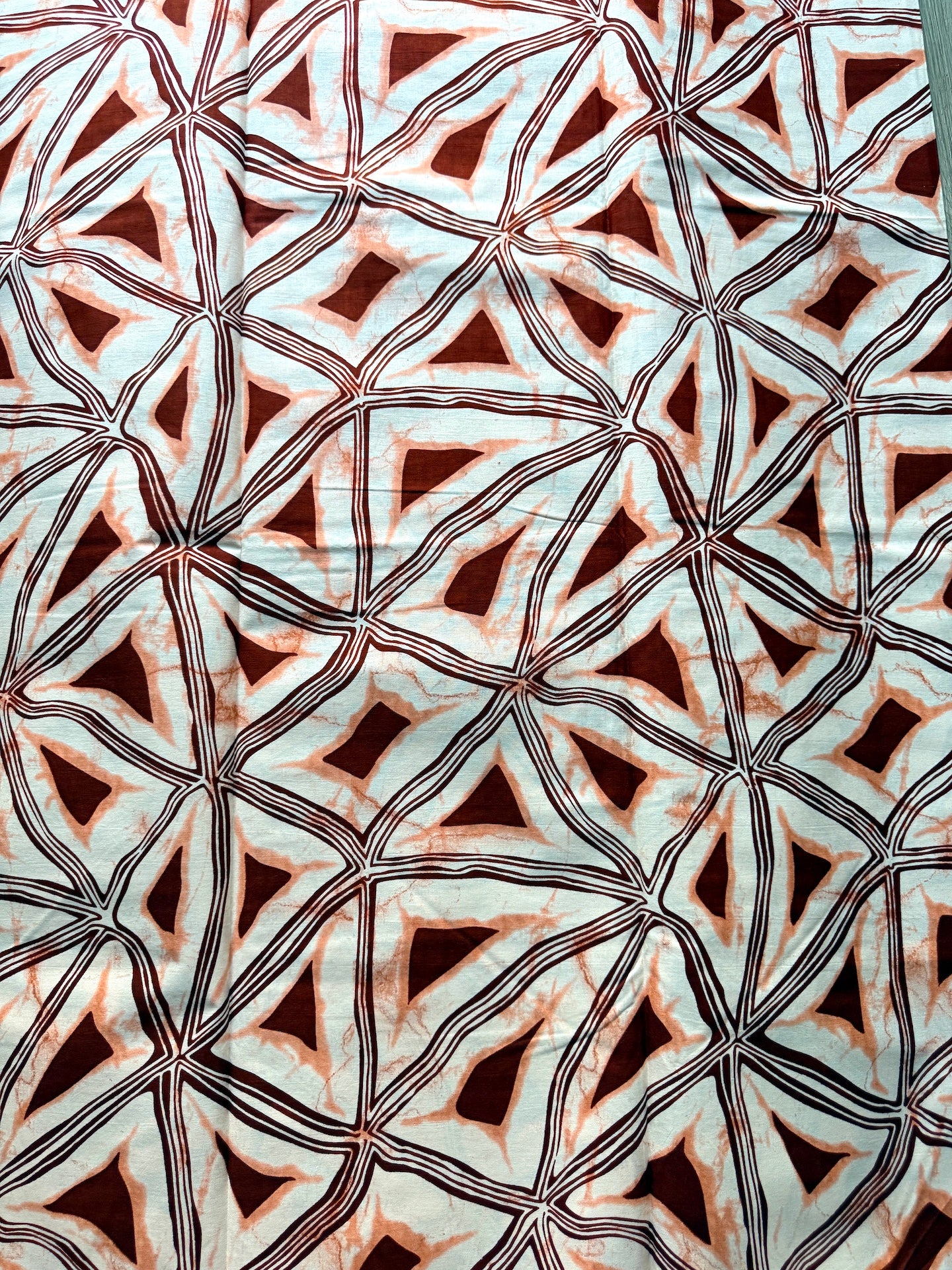 A close-up of patterned fabric with a repeating geometric design featuring dark brown triangles and black curved lines over a pale blue and white background.