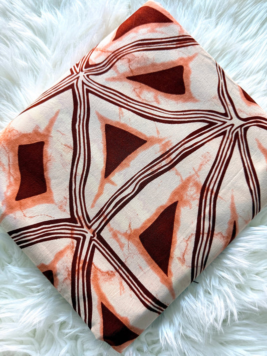 A square fabric pillow or cushion cover featuring a geometric pattern of terracotta orange triangles and dark brown lines on a cream background, styled on a white faux fur surface.