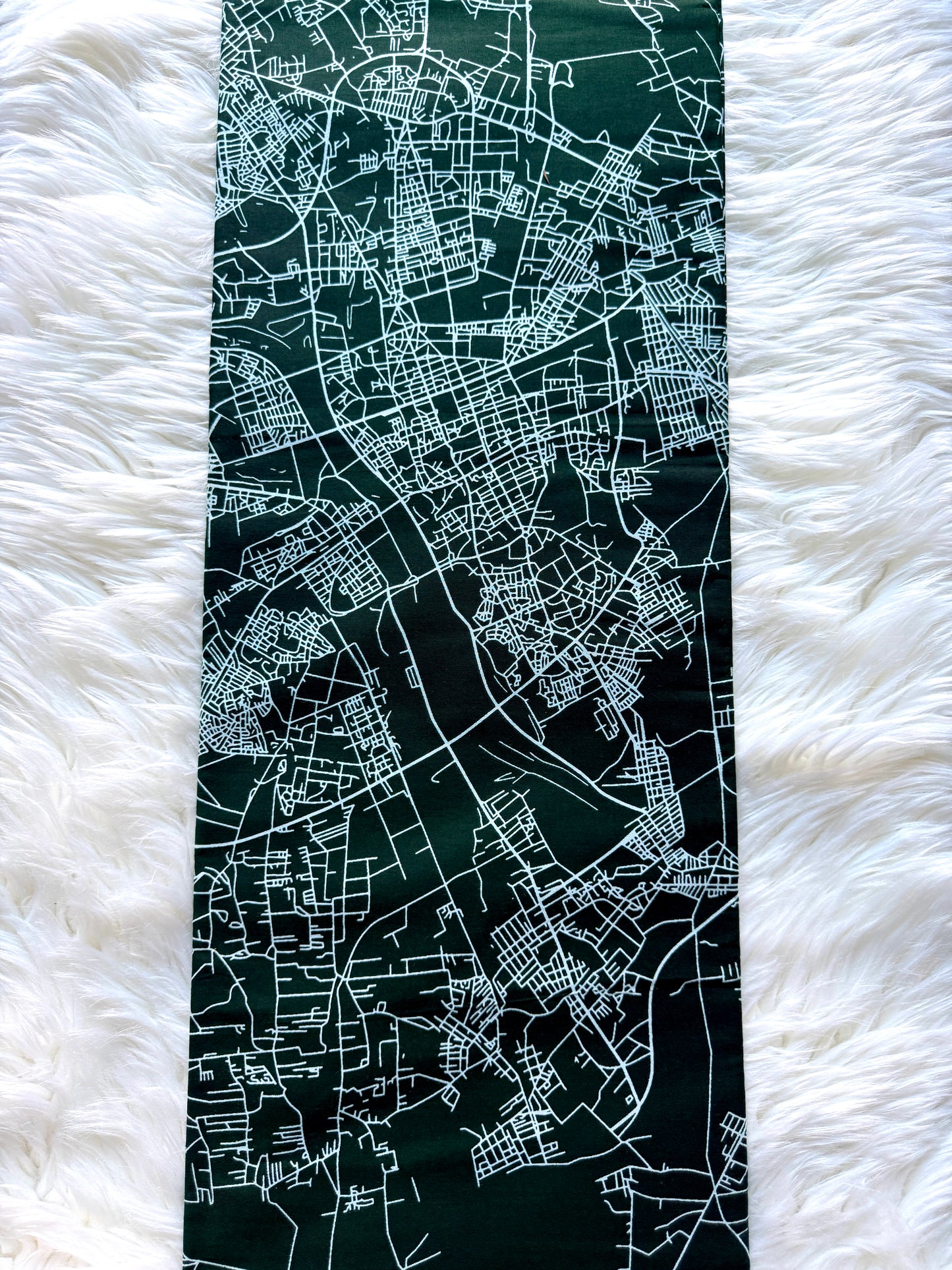 A long rectangular dark green scarf or bandana featuring a white street map print, laid flat on a white faux fur surface.