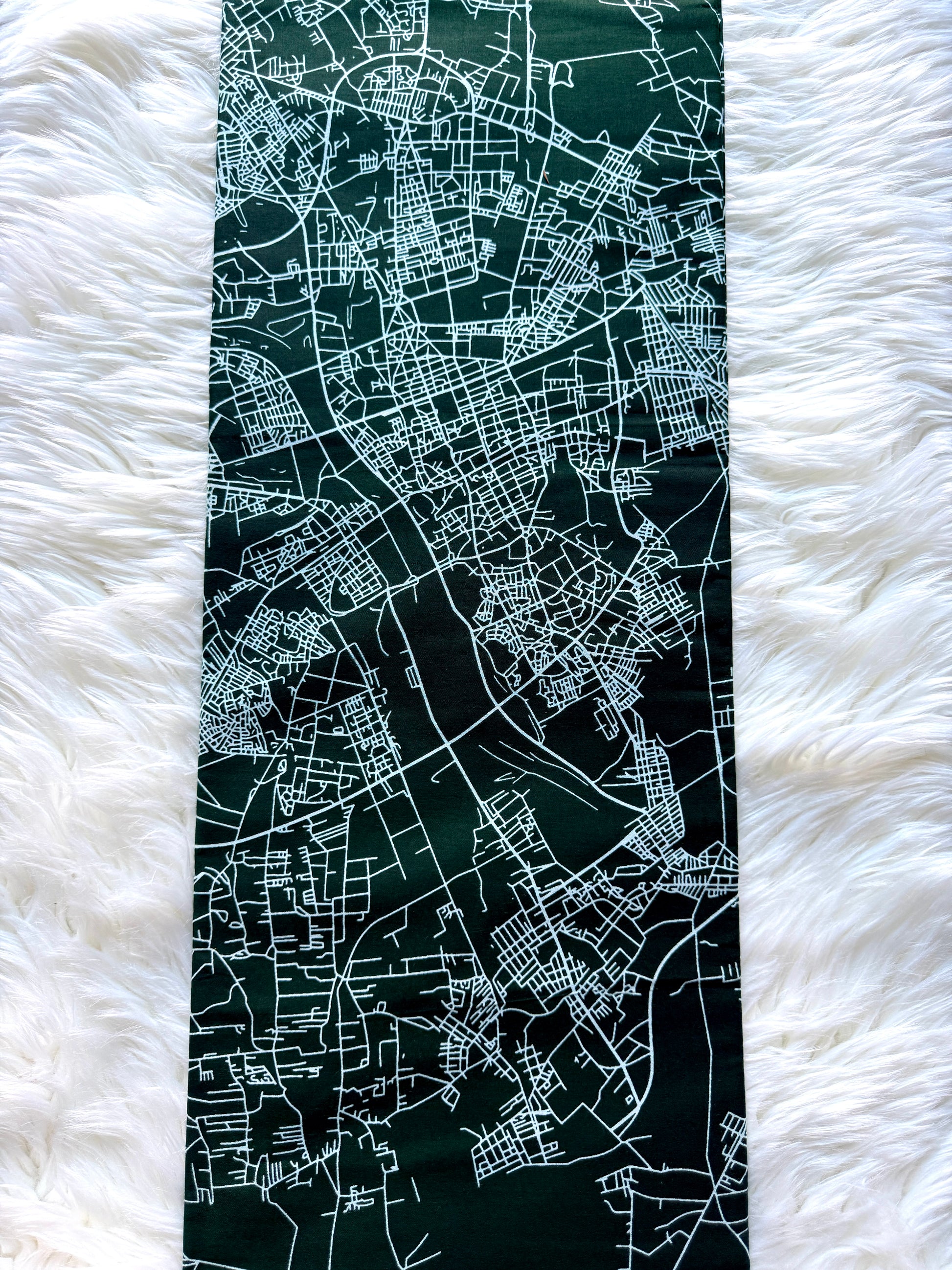 A long rectangular dark green scarf or bandana featuring a white street map print, laid flat on a white faux fur surface.