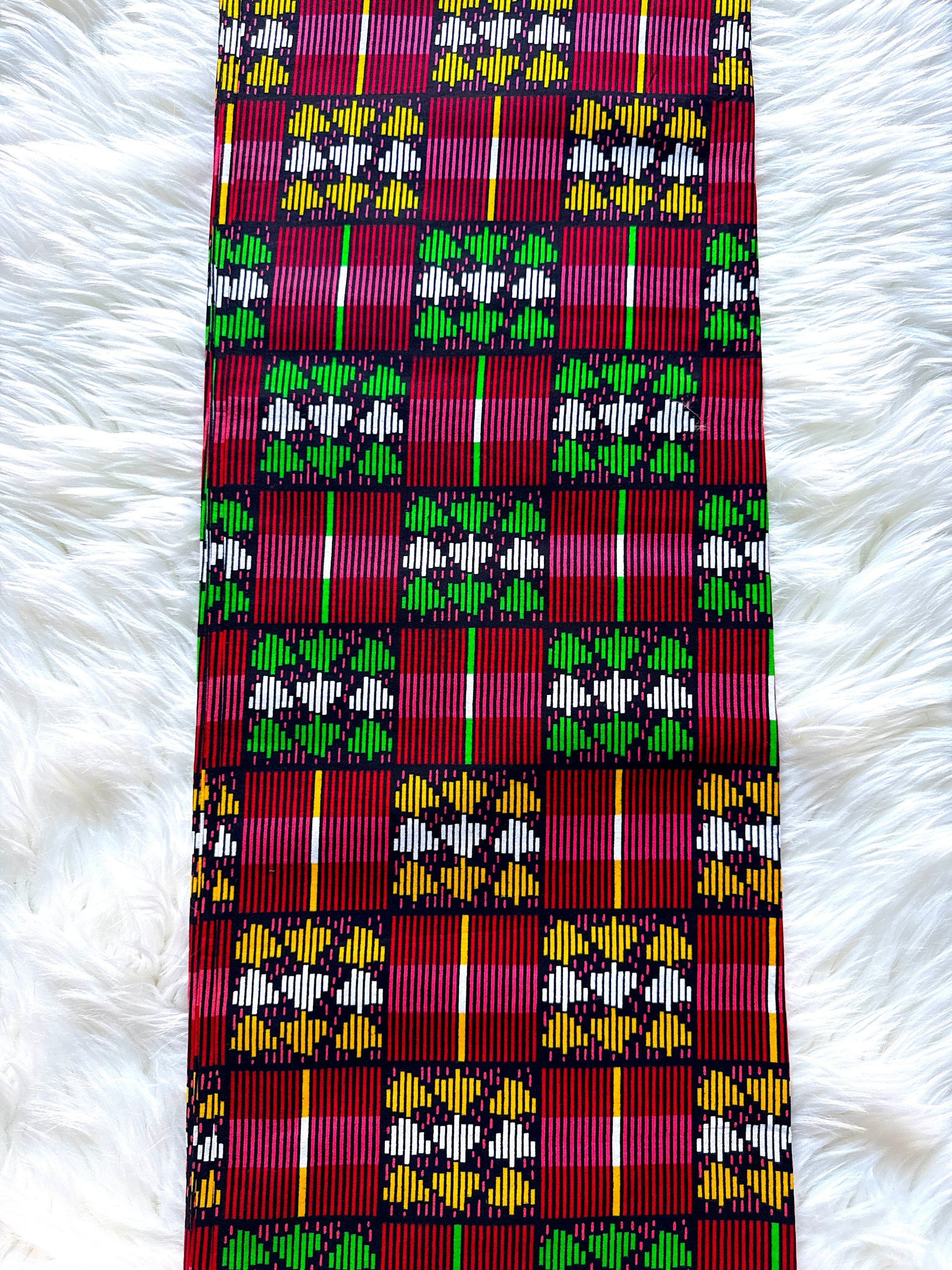 A close-up of a woven textile with a bold geometric pattern in magenta, green, white, yellow, and black, laid flat on a white faux fur background.