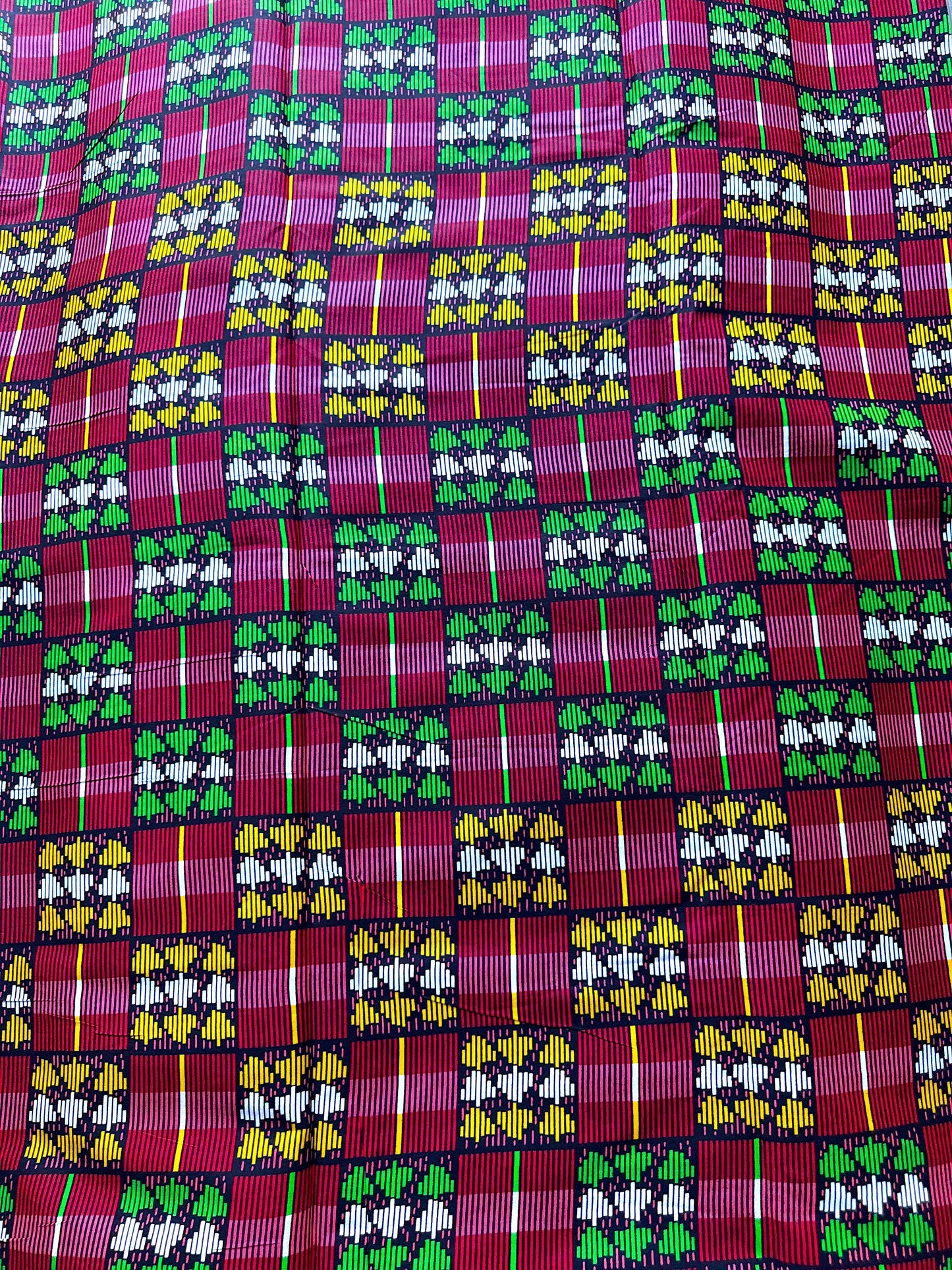 A close-up of a woven textile fabric featuring a vibrant African wax print pattern with magenta, green, yellow, and white geometric and floral motifs.