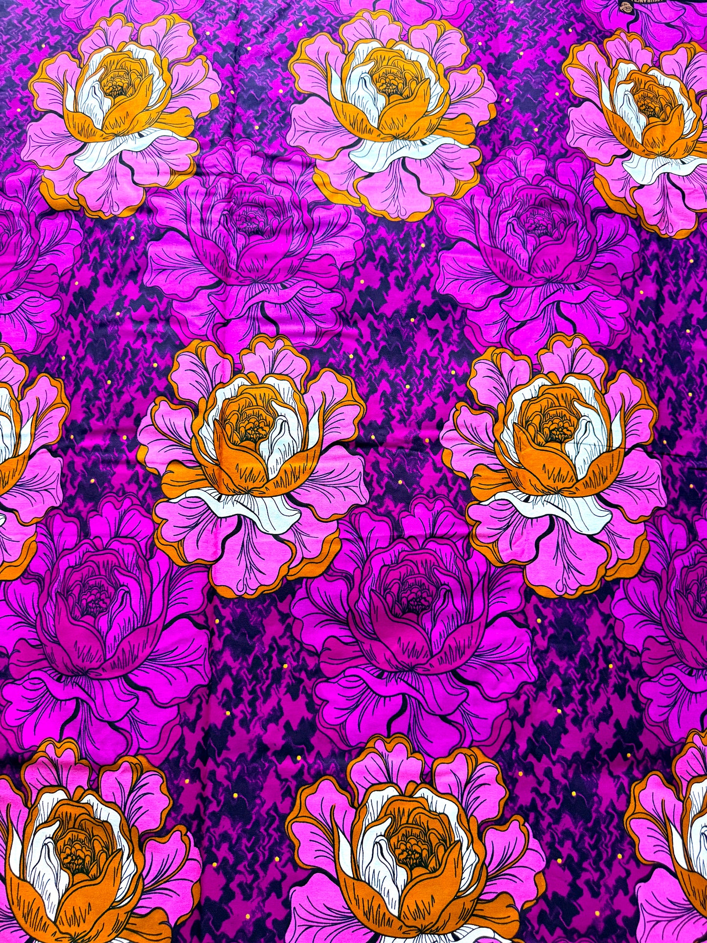 A close-up of a fabric pattern featuring large pink and white peony-like flowers with orange centers, set against a bright magenta and purple textured background.