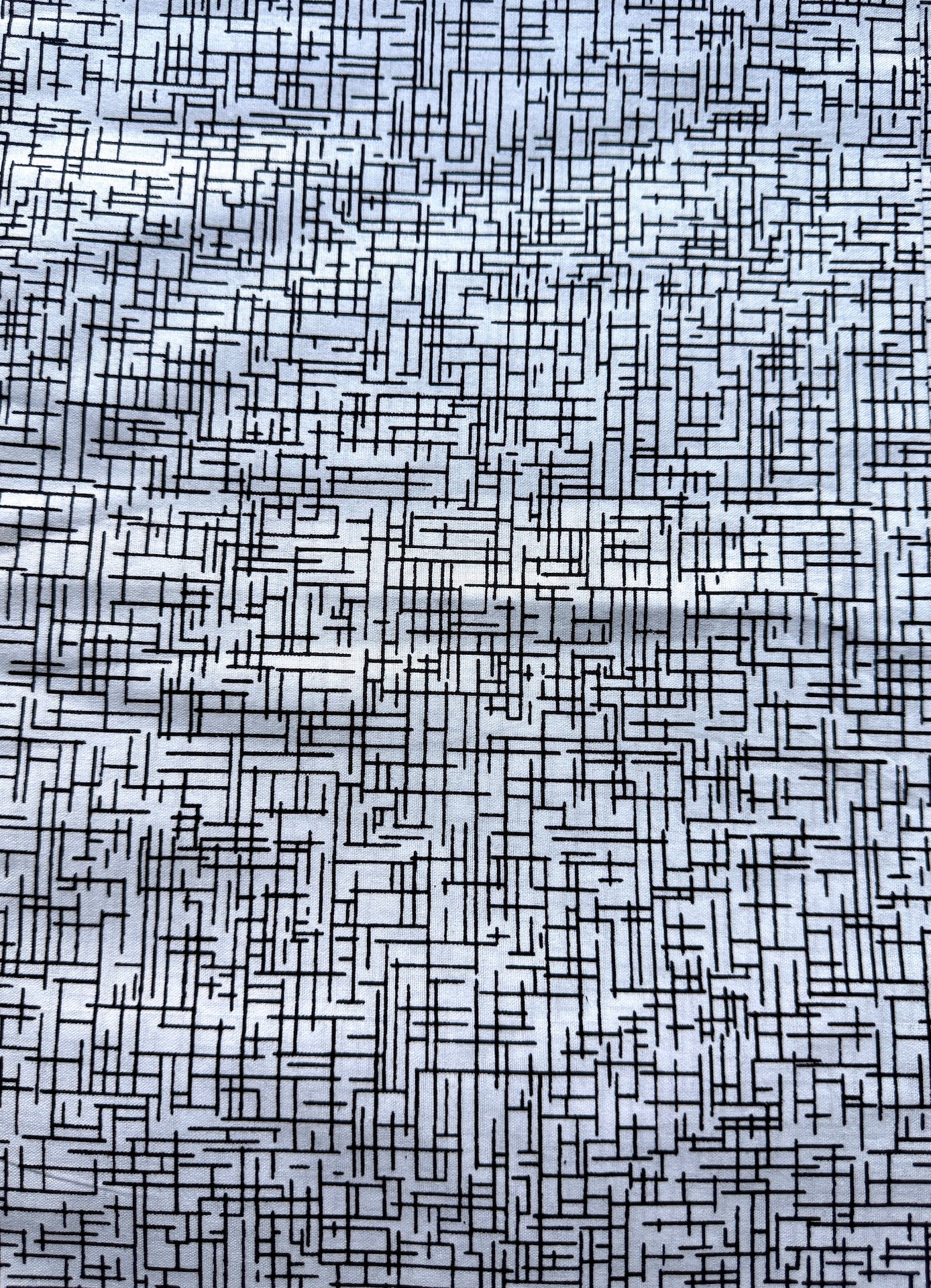 A close-up of a fabric or material surface with a dense black geometric maze-like line pattern on a light gray to white base.