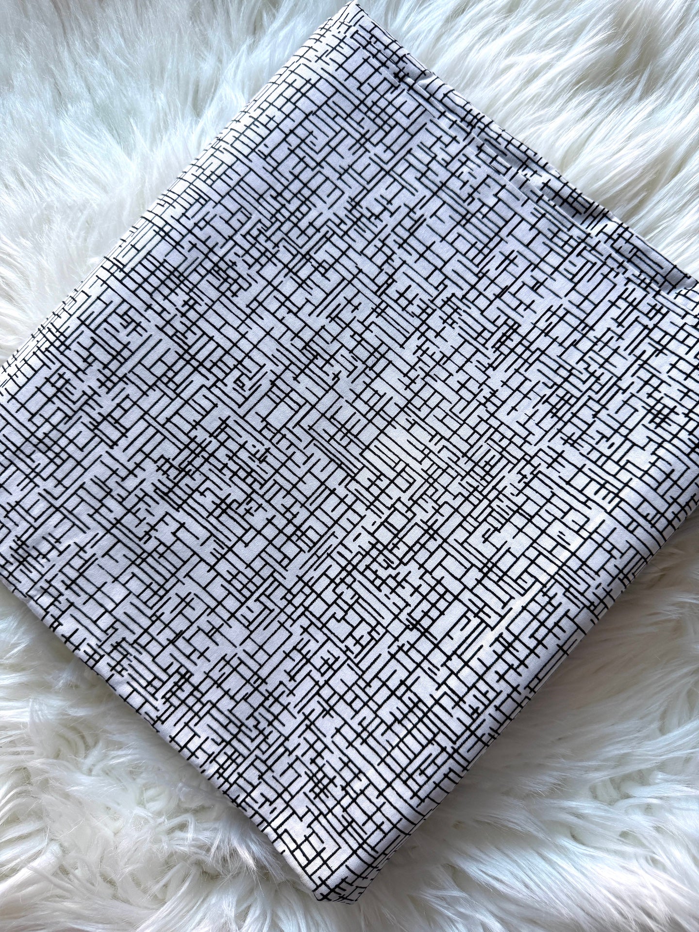 A square fabric pouch or small bag with a black and white geometric maze-like line pattern, laid flat on a white faux fur surface.
