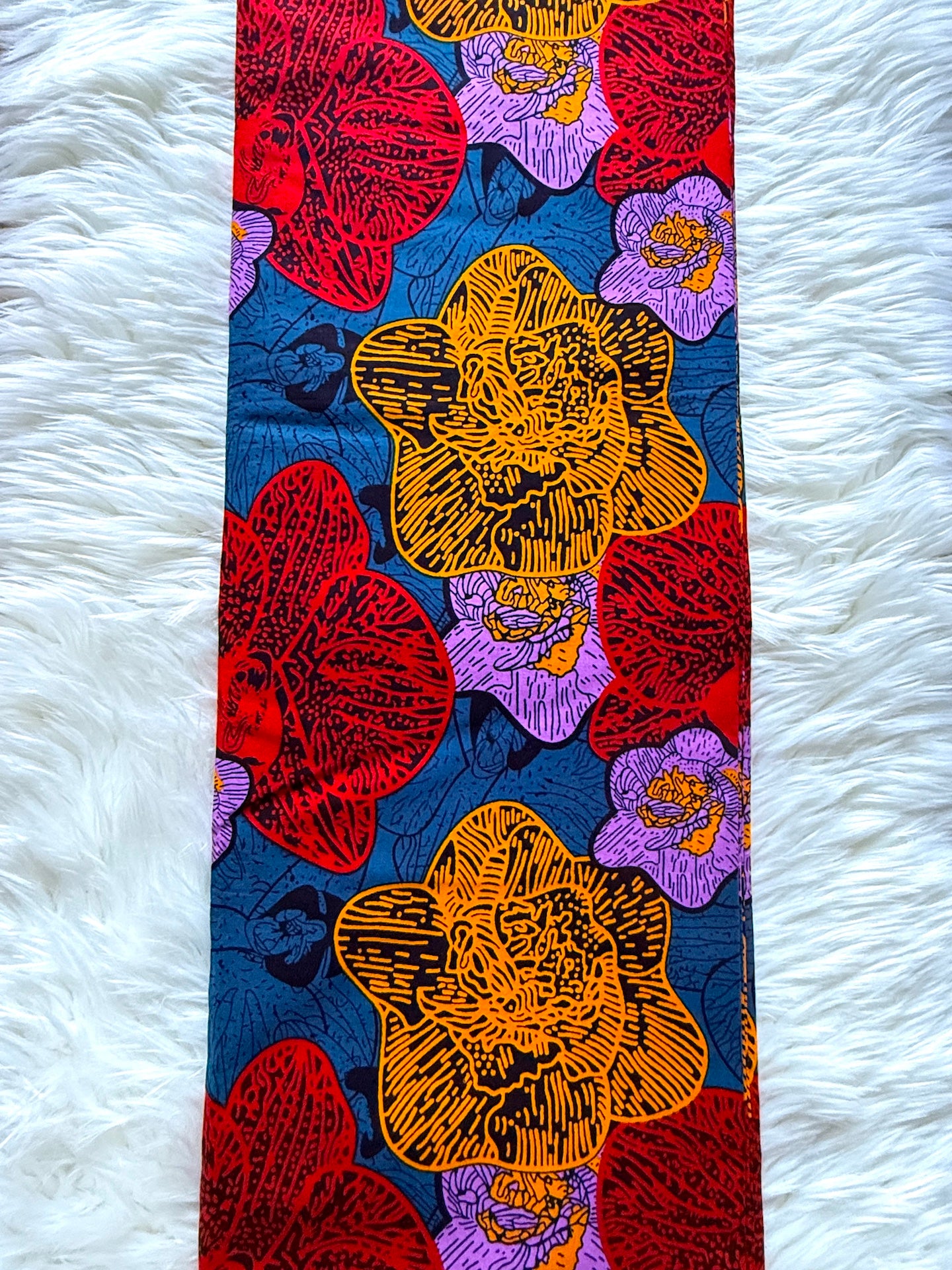 A vertical fabric panel featuring a vibrant floral pattern with red, yellow, and purple flowers on a dark blue background, laid flat on a white faux fur surface.