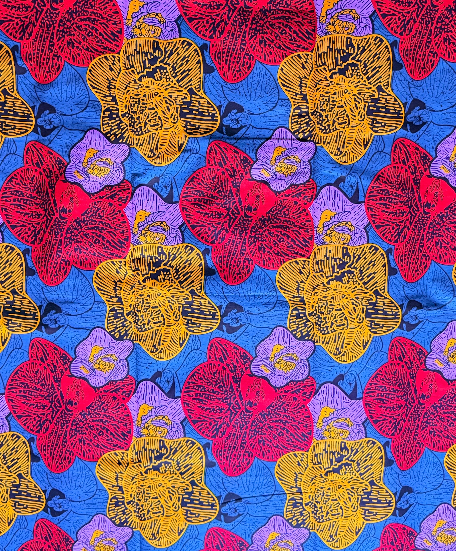 A close-up of a colorful floral fabric pattern featuring large red, yellow, and purple flowers on a bright blue background.