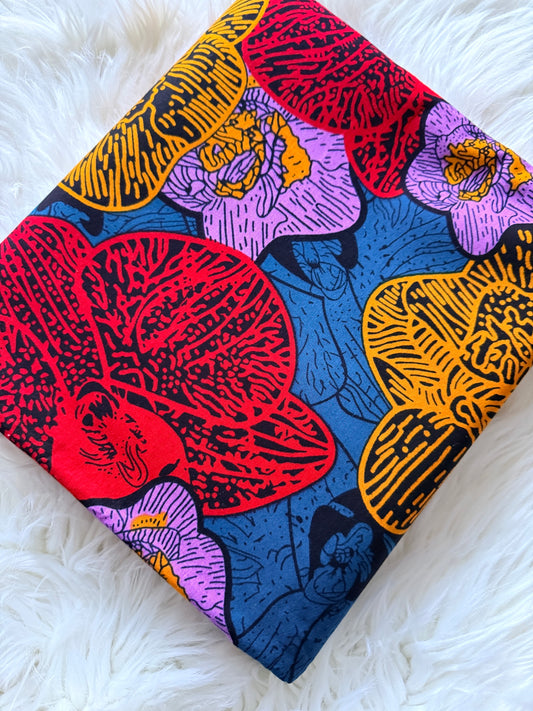 A square fabric item, likely a napkin or small scarf, featuring a vibrant floral pattern with red, purple, yellow, and blue flowers on a white faux fur background.