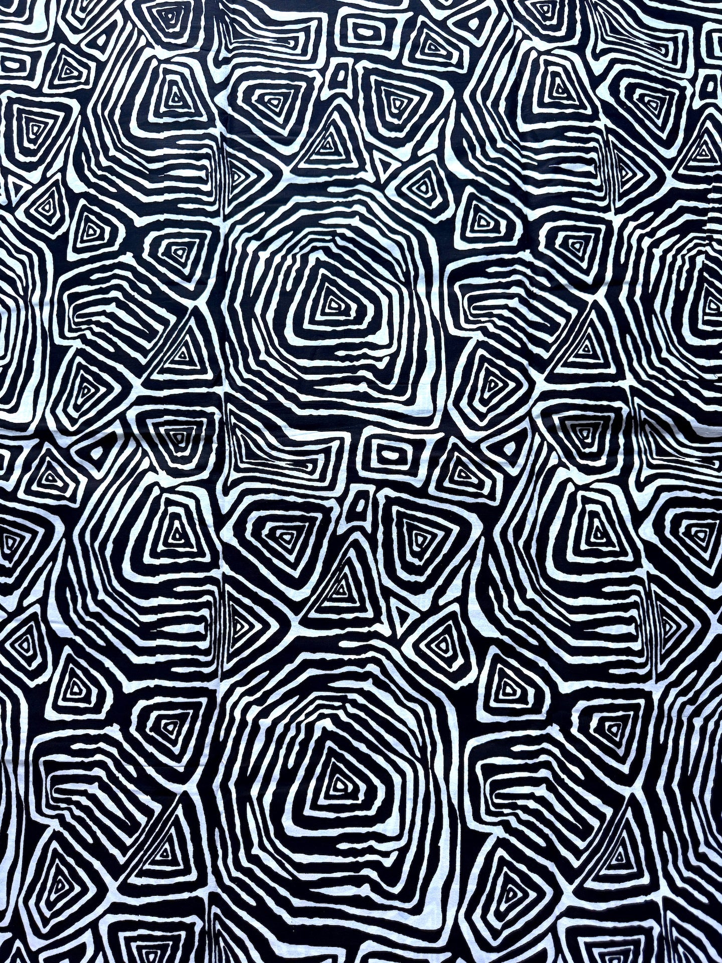 A close-up of a black and white fabric featuring an intricate, repeating geometric pattern of concentric triangles and irregular polygonal shapes.