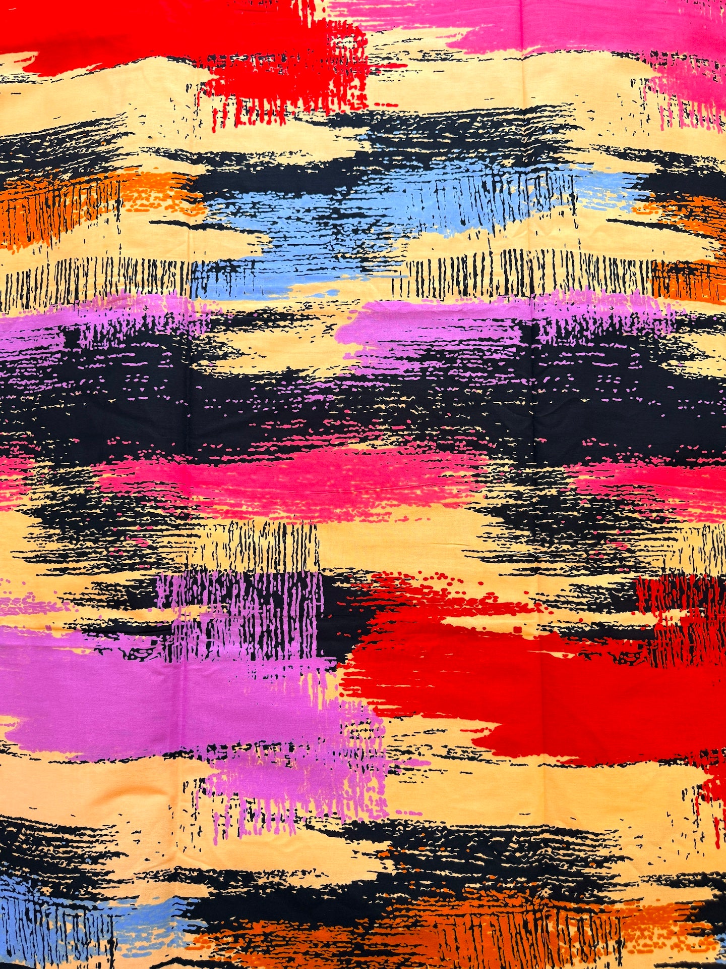 A close-up of a colorful abstract fabric pattern with broad brushstroke-like bands in black, magenta pink, red, purple, blue, orange, and beige.