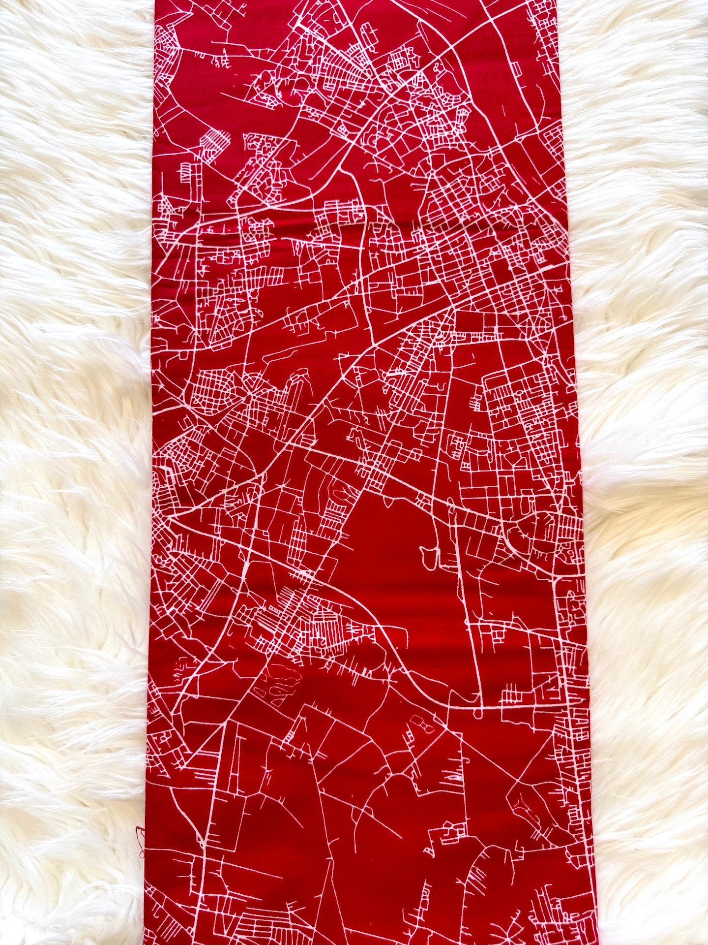 A red fabric runner or table runner with a white street map print, laid flat on a white faux fur surface.