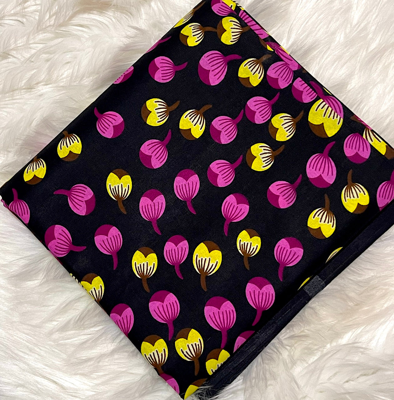 Patterned fabric with pink and yellow shapes on a black background, laid flat on a white textured surface.