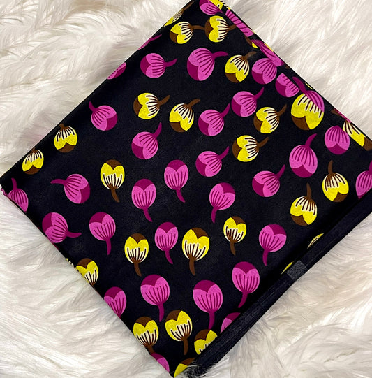 Patterned fabric with pink and yellow shapes on a black background, laid flat on a white textured surface.